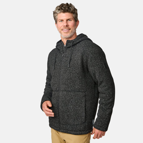 [Kolby is 6’2” wearing a size Medium.] Man wearing the Free Country Men's Northwood Mountain Fleece Hoodie in heather black with black drawstrings, standing with hands in pockets against a plain, light background.