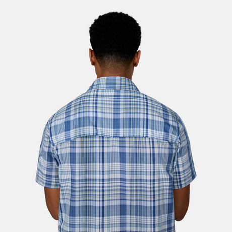 [Josiah is 6'3" wearing a size Medium.] Man wearing the Free Country Men's Excursion Short Sleeve Poplin Shirt in Denim Plaid, size M, made from lightweight moisture wicking polyester fabric featuring vent at the back, full button down front, and a stand collar, styled with navy shorts #color_ denim-plaid