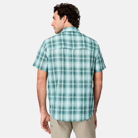 A man with curly brown hair is seen from the back wearing the Free Country Men's Excursion Short Sleeve Poplin Shirt in teal and white plaid, made of quick-dry, moisture-wicking fabric, paired with light khaki pants against a plain gray background.