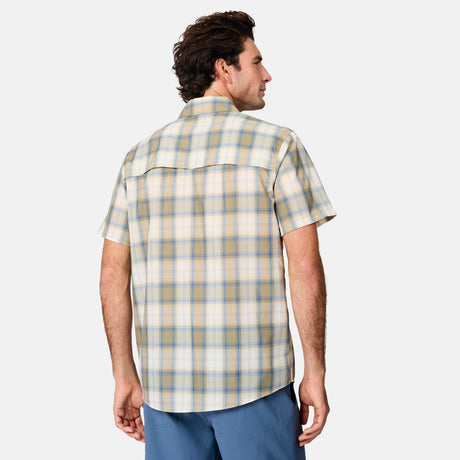 A man with dark hair, facing away, wears the Free Country Men's Excursion Short Sleeve Poplin Shirt in light yellow and blue plaid, paired with blue shorts against a plain light background.