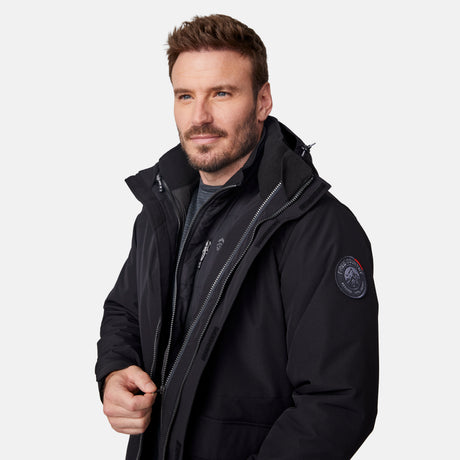 [Joe is 6’0” wearing size M.] Man wearing Free Country Men's Ski Patrol 3-in-1 Systems Jacket in black with a full front zipper opening, an outer jacket for wind and cold weather, an inner puffer jacket, and wind resistant and water resistant stretch performance fabric, light grey background. Perfect men’s jacket for winter weather.