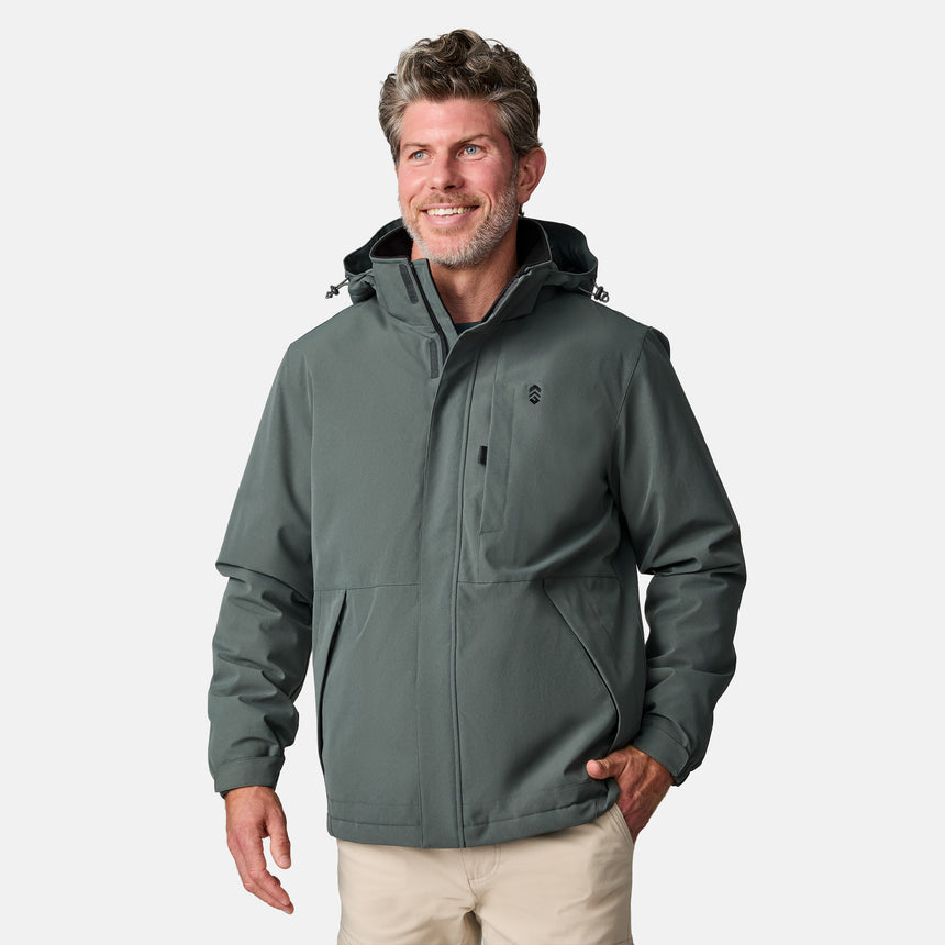 [Kolby is 6’2” wearing size M.]  "Men’s Free Country dark gray zip-front jacket with hood and chest pocket—layered over blue shirt and beige pants for a casual, transitional-weather look.