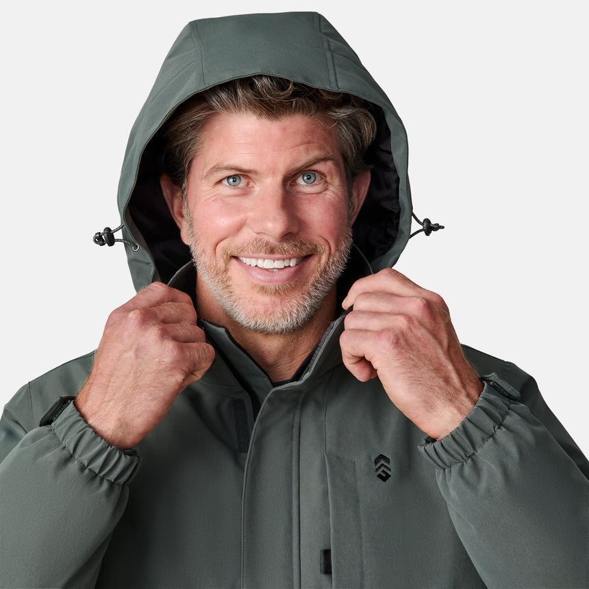 [Kolby is 6’2” wearing size M.]  "Men’s Free Country dark gray zip-front jacket with hood and chest pocket—layered over blue shirt and beige pants for a casual, transitional-weather look.