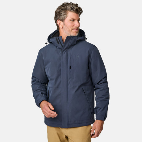 [Kolby is 6’2” wearing size M.] Men’s Free Country navy zip-front jacket with hood and high collar, featuring vertical chest zipper pocket and side hand pockets—worn over light brown pants for an outdoors-ready, insulated look.