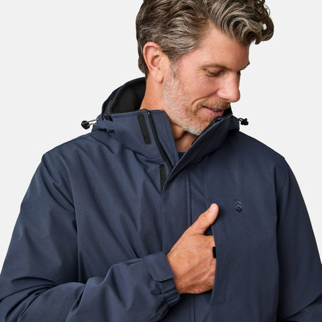 [Kolby is 6’2” wearing size M.] Men’s Free Country navy zip-front jacket with hood and high collar, featuring vertical chest zipper pocket and side hand pockets—worn over light brown pants for an outdoors-ready, insulated look.