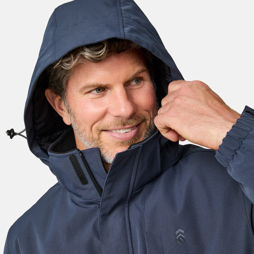 [Kolby is 6’2” wearing size M.] Men’s Free Country navy zip-front jacket with hood and high collar, featuring vertical chest zipper pocket and side hand pockets—worn over light brown pants for an outdoors-ready, insulated look.