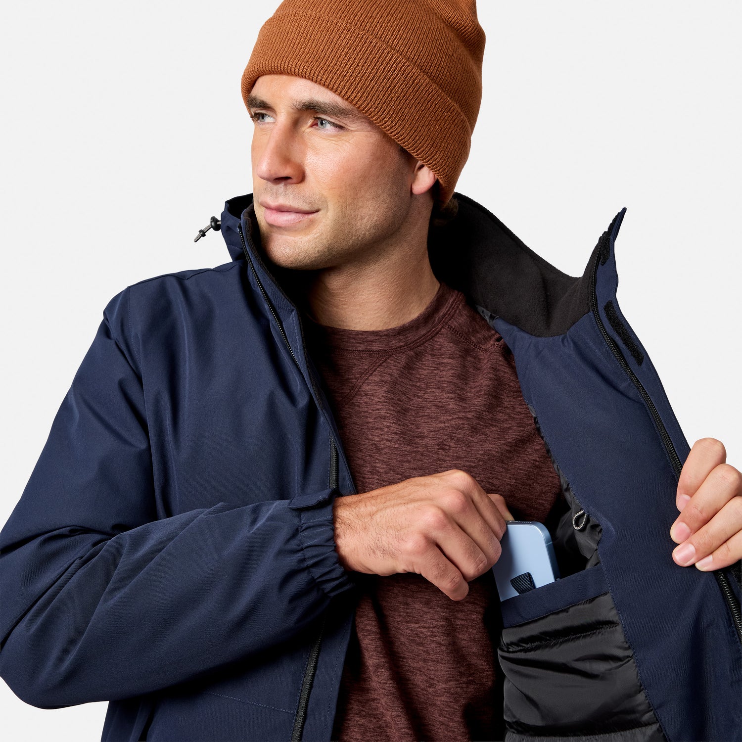 Portrait of a man wearing a rust knit beanie and navy Denali insulated jacket with a front zipper.