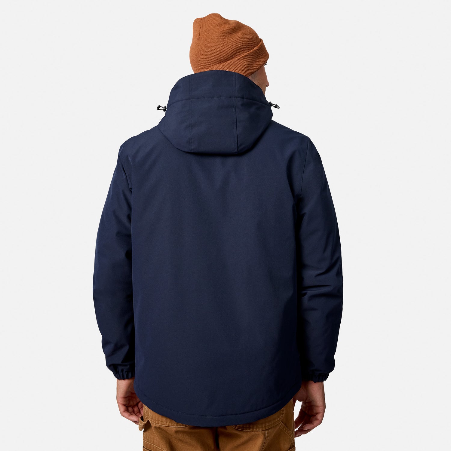 Back angle of a man wearing a navy Denali insulated jacket with the hood down and a rust beanie, brown pants visible.