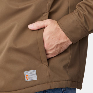 [Joe is 6'0" wearing size M.] Men’s Free Country brown canvas jacket layered over a white crewneck tee and blue jeans—features zippered chest pockets and left-side logo patch for rugged outdoor appeal and everyday versatility.