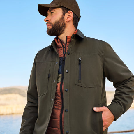 Man wearing a green jacket and cap outdoors with a clear blue sky.