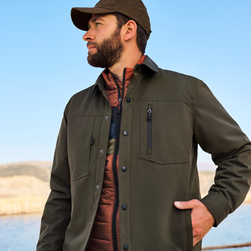 Man wearing a green jacket and cap outdoors with a clear blue sky.