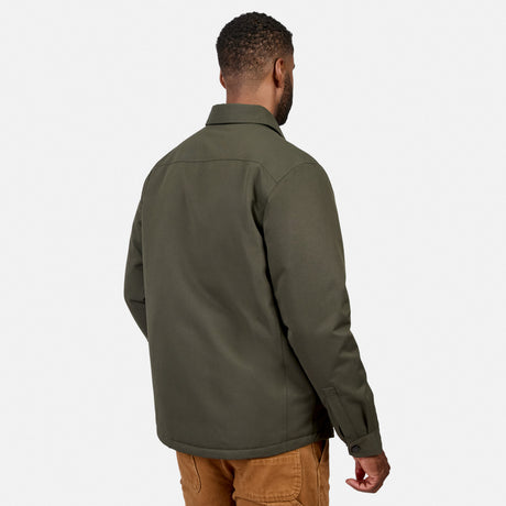 A man stands facing away, wearing the Free Country Men’s Brawny Canvas Function Work Jacket in olive green and brown pants, against a plain white background.