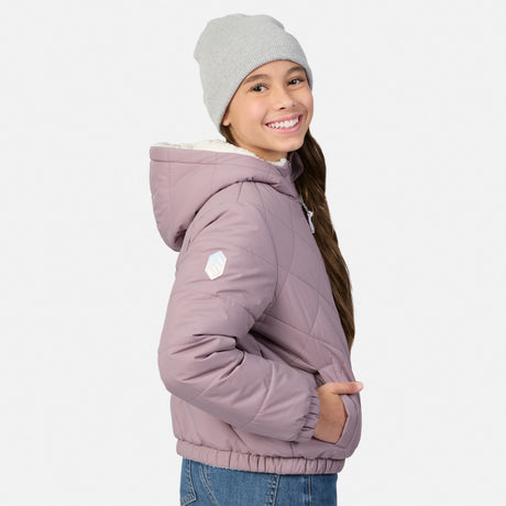 A young girl wearing a light gray knit beanie and a dusty purple quilted puffer jacket with a white hood lining, shown from a side-back angle against a light gray studio background.