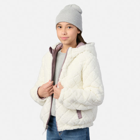 A young girl wearing a white quilted sherpa fleece hooded jacket with a gray beanie, gray t-shirt, and blue jeans, standing against a light gray studio background.