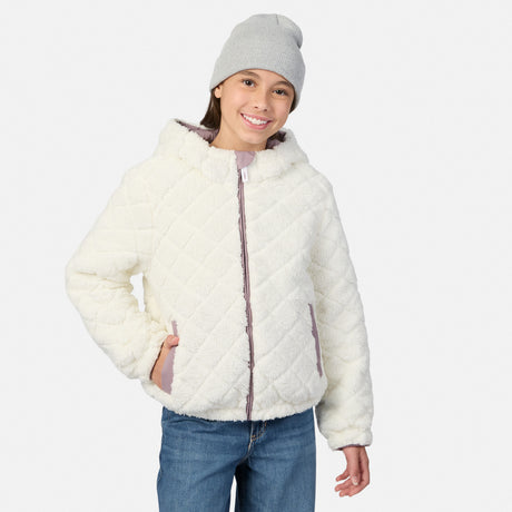 A young girl wearing a cream-colored, diamond-quilted fleece jacket with a gray beanie and blue jeans, standing against a light gray studio background.