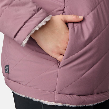 A hand is partially tucked into the pocket of a Women's Plus Size Cirrus Quilted Reversible Jacket by Clearance, featuring mauve quilting, soft white lining, REPREVE insulation, visible diagonal stitching, and a small logo near the hem.
