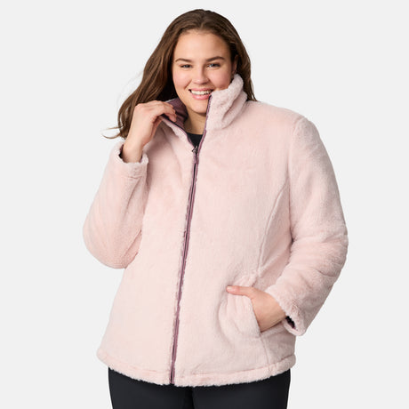A woman smiles at the camera against a white background, wearing the Clearance Women's Plus Size Cirrus Quilted Reversible Jacket in light pink, her left hand in a pocket and right hand touching the collar.