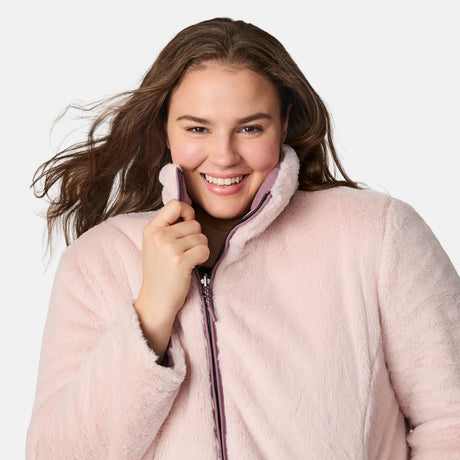 A smiling woman with long brown hair wears the Women's Plus Size Cirrus Quilted Reversible Jacket by Clearance, holding the collar and looking at the camera against a plain white background.