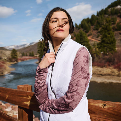 Woman standing outdoors with a scenic background of mountains and a lake.