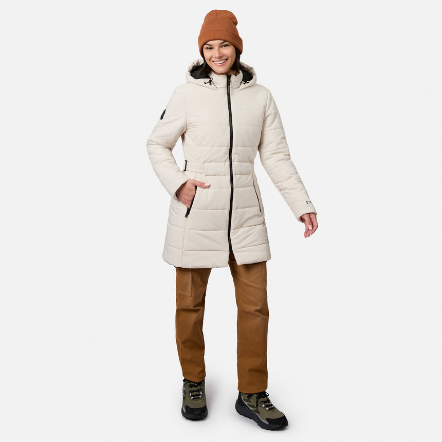 A woman wearing an off-white, water-resistant Women’s Cirrus Quilted Long Puffer Jacket, brown beanie, brown pants, and olive-green hiking sneakers.
