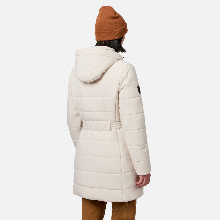 Back view of a person wearing a cream-colored Free Country Women’s Cirrus Quilted Long Puffer Jacket, featuring a water-resistant, long, hooded quilted design with a belted waist.
