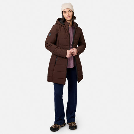 A person wearing a brown Women’s Cirrus Quilted Long Puffer Jacket with REPREVE insulation, a maroon shirt, dark blue trousers, and a beanie.