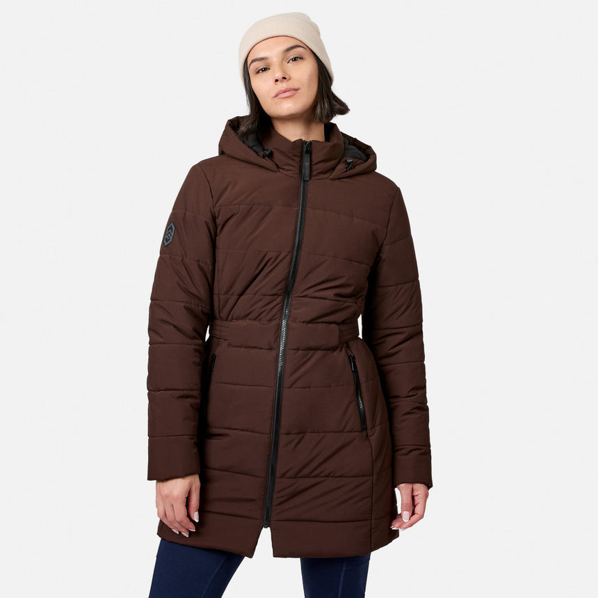 A woman wearing an espresso-colored Women’s Cirrus Quilted Long Puffer Jacket, a dark brown recycled polyester hooded coat with a front zipper and belted waist.