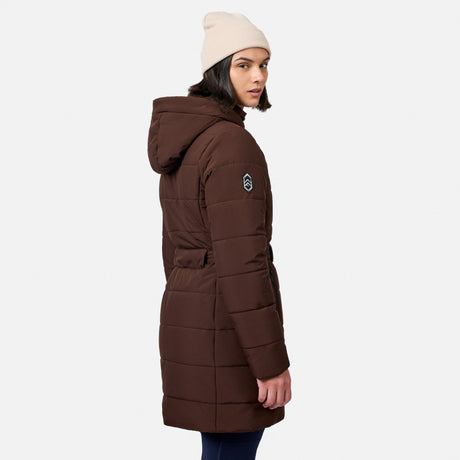 A woman wearing a brown Free Country Women’s Cirrus Quilted Long Puffer Jacket with recycled insulation and a beige beanie looking over her shoulder.