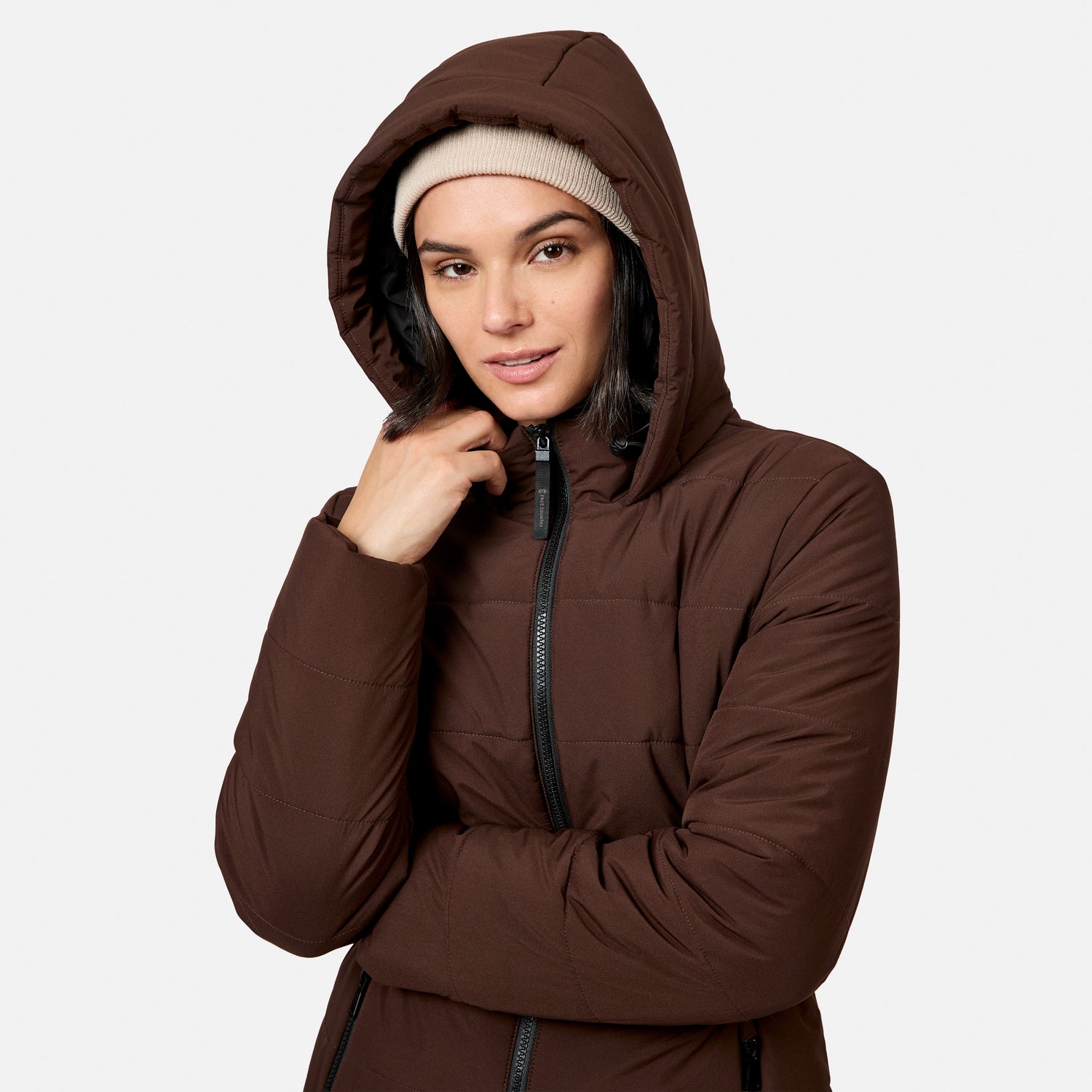 A person wearing a brown Women’s Cirrus Quilted Long Puffer Jacket with REPREVE insulation and a beige beanie.