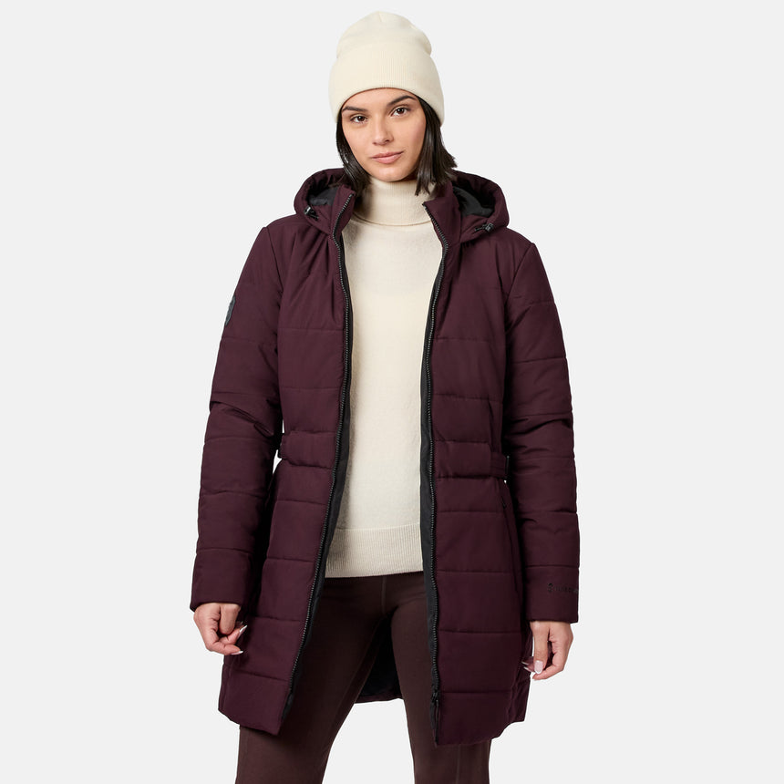 A woman wearing a dark burgundy Women’s Cirrus Quilted Long Puffer Jacket over a cream turtleneck sweater and a matching beanie.