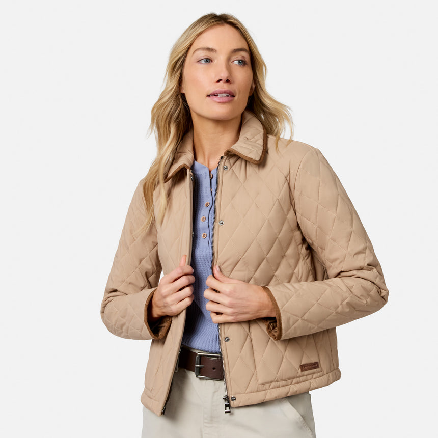 [Model is wearing size S.] A woman wearing a beige diamond-quilted jacket over a light blue knit top and khaki pants, photographed against a clean light gray studio background.