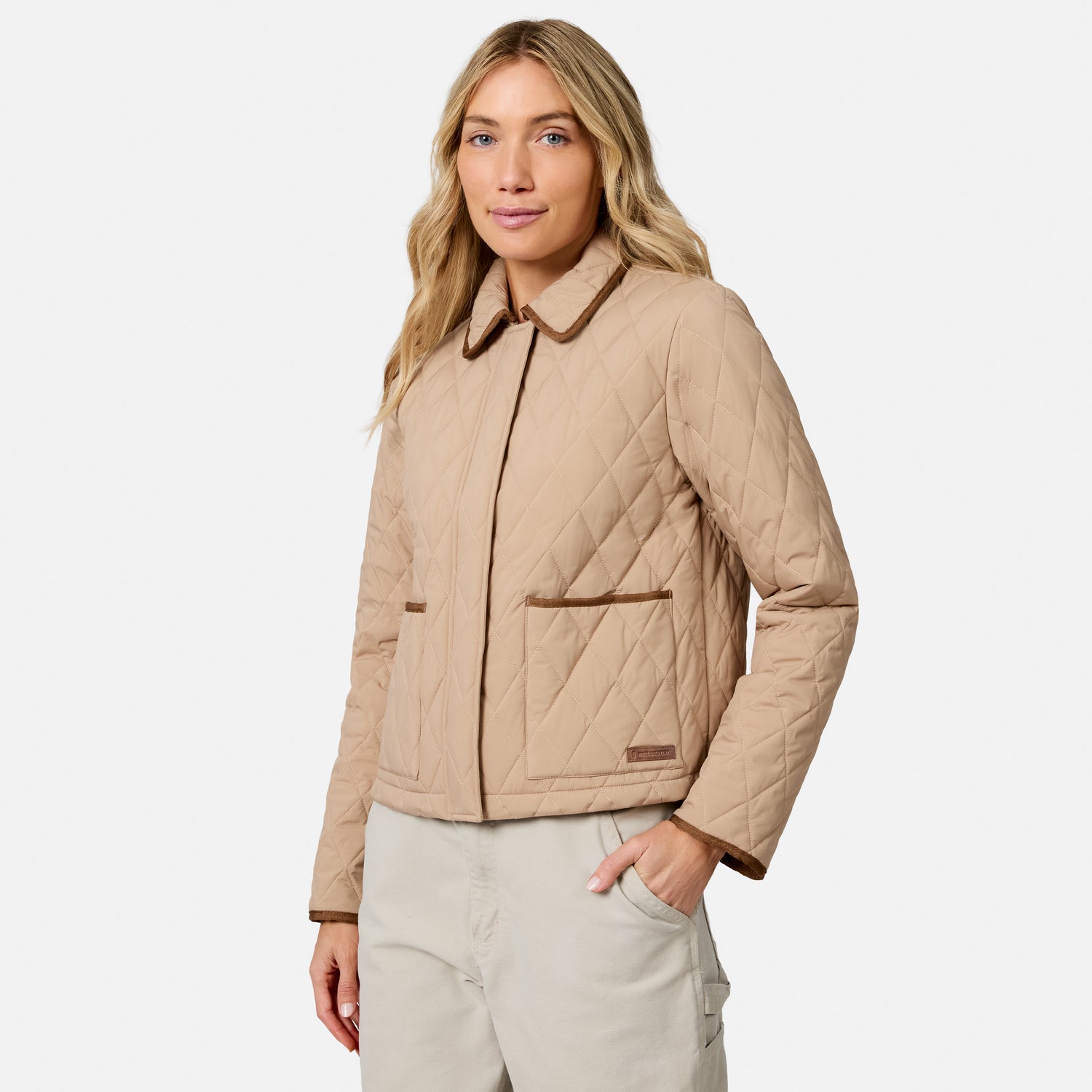 [Model is wearing size S.] A woman modeling a light tan quilted jacket with brown trim, paired with light beige pants, against a solid light gray background.