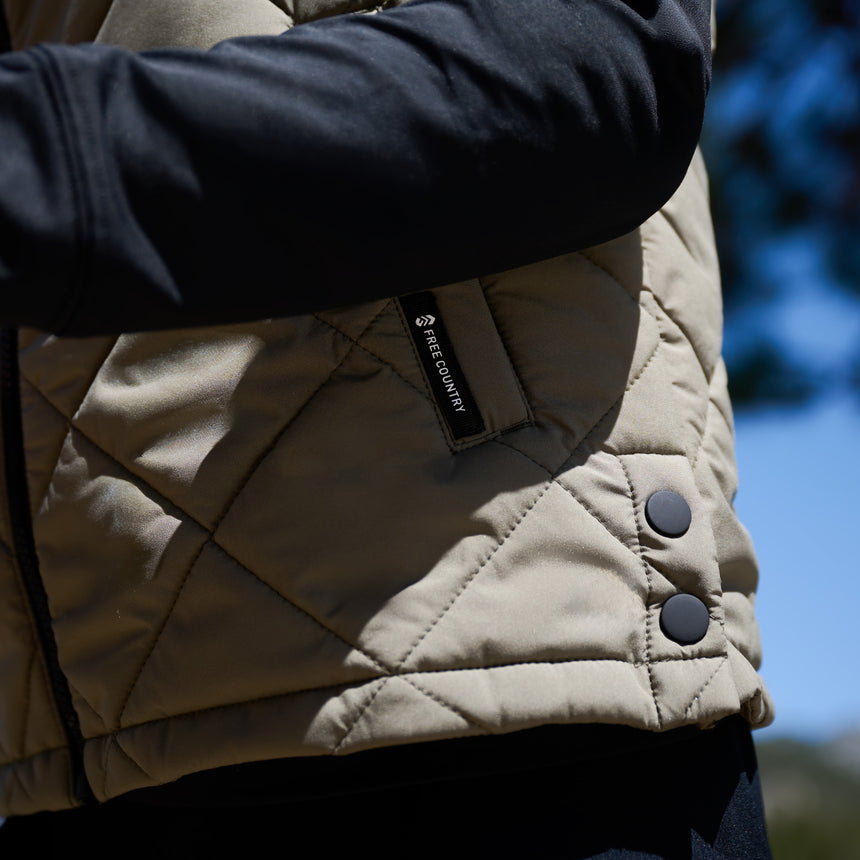 Close up of the hemline of a green quilted Free Country vest, with a Fee Country logo visible on the pocket