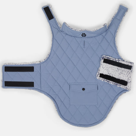 The Clearance Stratus Lite Reversible Dog Jacket is light blue, wind resistant, quilted, and features black Velcro straps, white fleece lining, a small front pocket, and a matching detachable rectangular Velcro patch.