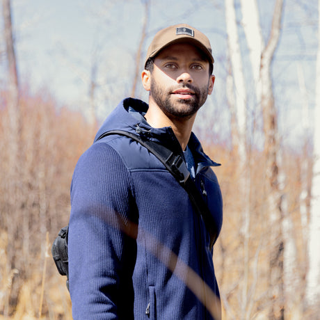 Man wearing a blue Free Country fleece jacket and brown cap outdoors with trees in the background