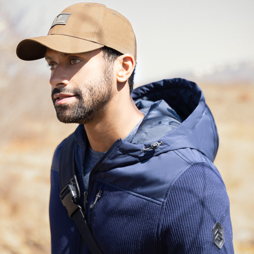 Man wearing a blue Free Country fleece jacket and brown cap outdoors with trees in the background