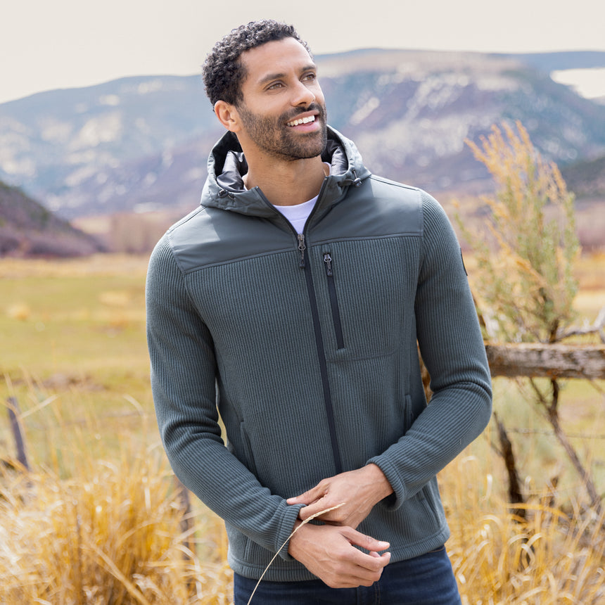 Man wearing a green fleece Free Country jacket in a natural setting with mountains and grass.