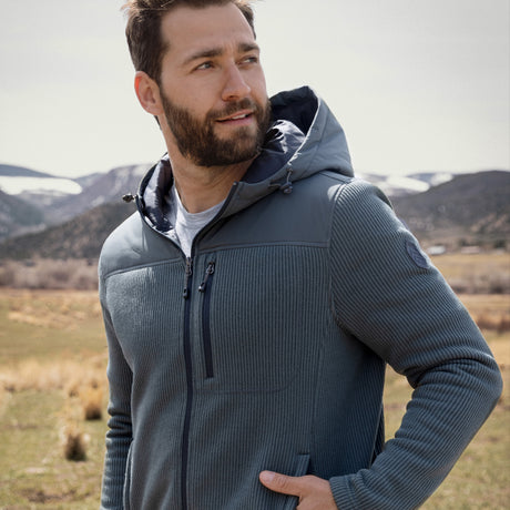 Man wearing a green fleece Free Country jacket in a natural setting with mountains and grass.