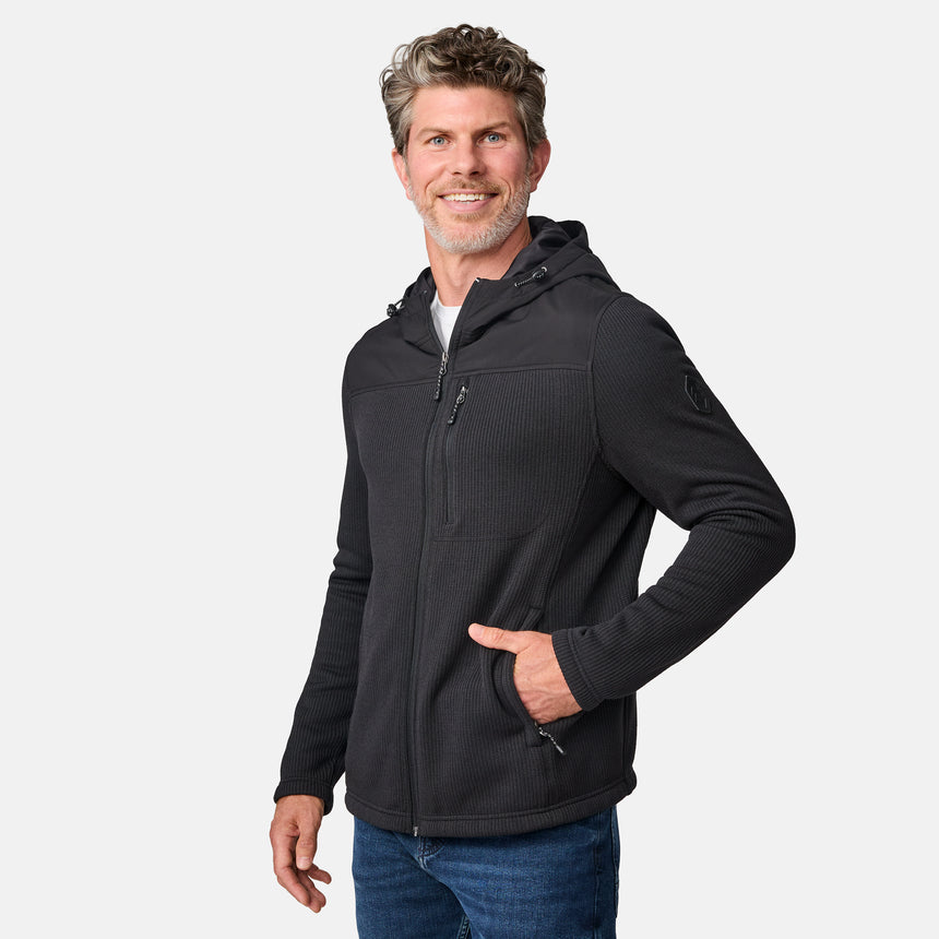 [Kolby is 6'2" wearing size M.] Men’s Free Country dark grey hooded jacket with full-zip front, zippered chest pocket, and dual side hand pockets—featuring textured fabric and a clean outdoor silhouette. Paired with beige pants for a rugged, cool-weather look.