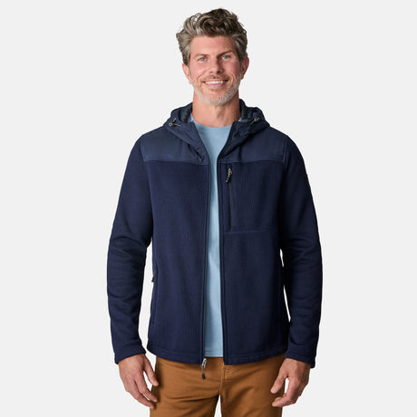 [Kolby is 6'2" wearing size M.] Men’s Free Country navy blue hooded jacket with full-zip front, zippered chest pocket, and dual side hand pockets—featuring textured fabric and a clean outdoor silhouette. Paired with beige pants for a rugged, cool-weather look.