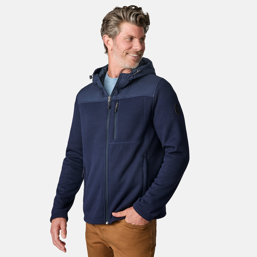 [Kolby is 6'2" wearing size M.] Men’s Free Country navy blue hooded jacket with full-zip front, zippered chest pocket, and dual side hand pockets—featuring textured fabric and a clean outdoor silhouette. Paired with beige pants for a rugged, cool-weather look.