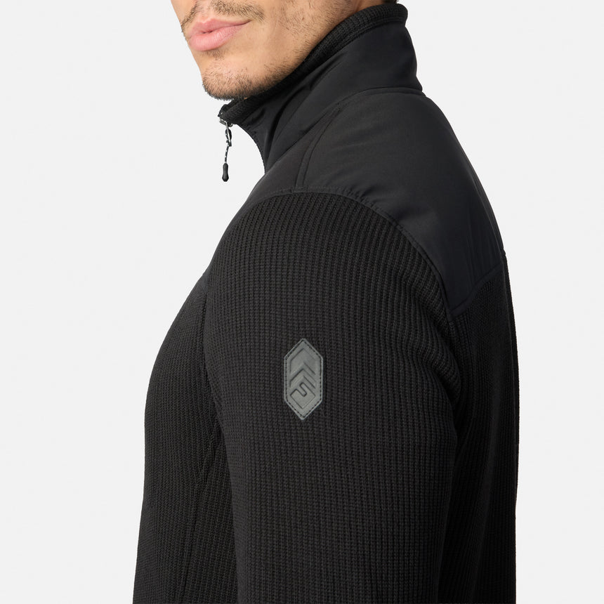 [Model is wearing size M.] A close-up side view of a man wearing a black quarter-zip pullover jacket with a textured waffle-knit sleeve and a gray shield logo patch on the upper arm, set against a plain light gray background.