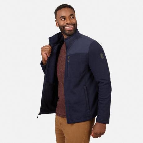 [Model is wearing size M.] A man wearing a navy blue zip-up fleece jacket with a ribbed chest panel, styled over a brown sweater and tan pants, photographed against a light gray studio background.