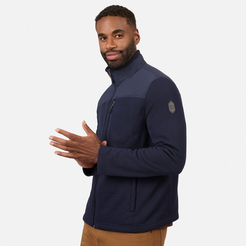 [Model is wearing size M.] A man wearing a navy blue ribbed zip-up jacket with dark navy shoulder panels, standing against a light gray background.