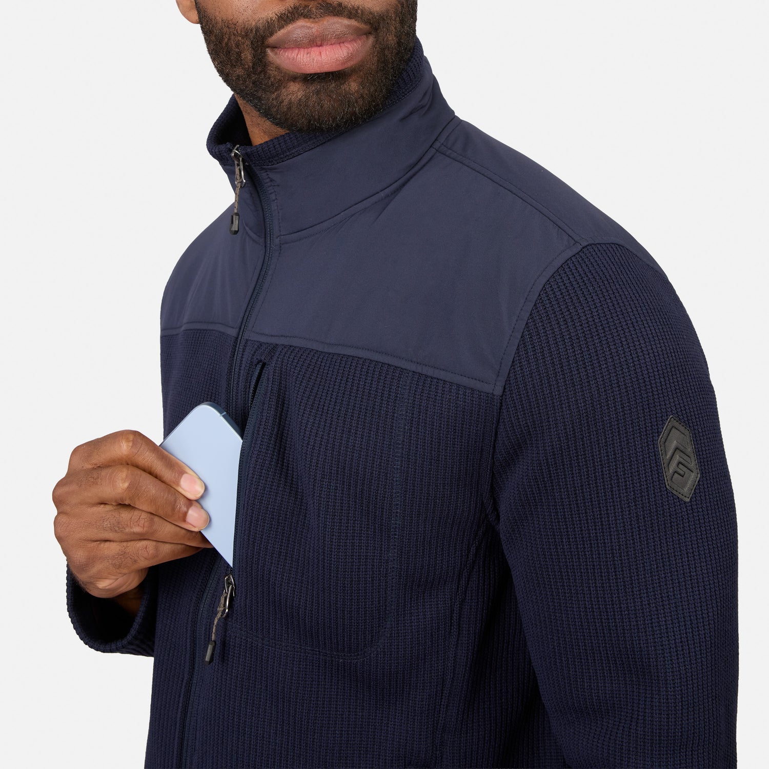 [Model is wearing size M.] A close-up of a man wearing a navy blue quarter-zip fleece jacket with a textured knit lower section and a dark sleeve patch, holding a light blue card.