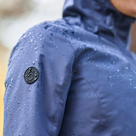 Close up of a dark blue rain jacket repelling droplets of water with a black Free Country logo