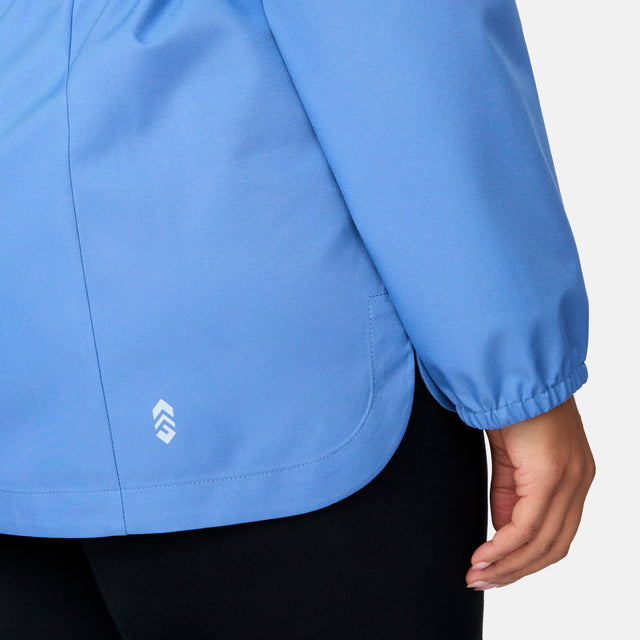A person’s right arm and hip wearing the Free Country Women's Plus Size X2O Anorak Rain Jacket in light blue, featuring an elastic cuff and a small white logo near the hem, paired with black pants against a plain background.