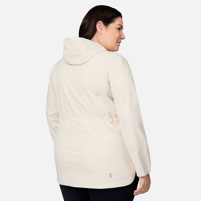 A woman with dark hair, wearing the Free Country Women's Plus Size X2O Anorak Rain Jacket in a light color and black pants, stands facing away against a plain white background.