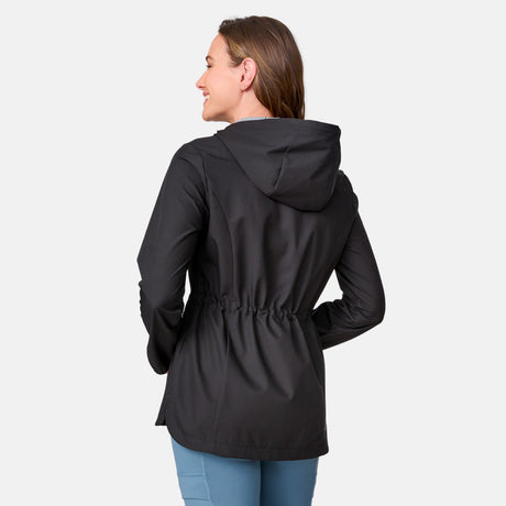 A woman with brown hair, smiling and facing away, wears the Free Country Women's X2O Anorak Rain Jacket in black with a cinched waist, paired with light blue pants, against a plain light background.