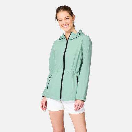 A woman smiles wearing the Free Country Women's X2O Anorak Rain Jacket in light green and white shorts, standing against a plain light background.